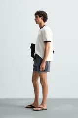 Bañador largo de hombre color rosa pálido con textura seersucker. Presenta cintura elástica ajustable con cordón blanco, bolsillos laterales y un bolsillo trasero de plastrón.