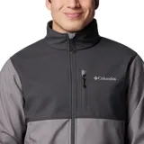 Chaqueta Columbia Ascender Soft Shell con diseño bicolor en tonos gris y gris oscuro. Cuenta con cierre frontal completo, cuello alto con protector de mentón, bolsillo en el pecho con cierre, bolsillos laterales con cierre y puños ajustables con velcro.