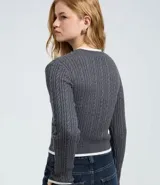 Sweater cropped de punto gris con diseño trenzado, cuello redondo, puños y ruedo con ribetes blancos. Presenta un aplique bordado en el pecho con diseño de osito deportista.