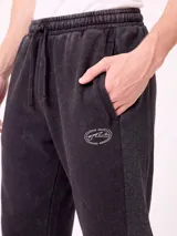 Pantalón jogger holgado de color gris con efecto acid wash y franjas laterales negras. Cuenta con cintura elástica con cordón ajustable y bolsillos laterales.