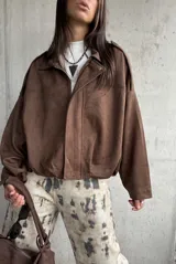 Campera tipo bomber de gamuza color chocolate, con diseño oversize, mangas amplias y apliques decorativos en los hombros. Cuenta con cierre frontal y forro interior.