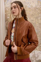 Chaqueta de cuero estilo bomber, con cuello alto, puños y cintura de tejido de punto acanalado. Presenta cierre frontal con cremallera y dos bolsillos laterales con solapa.