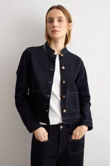 Chaqueta de jean azul oscuro, con cuello mao, cierre frontal de botones metálicos y dos bolsillos frontales de parche.