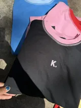 Buzo deportivo de verano (sin felpa) color negro, corte oversize, con cuello redondo y pespuntes contrastantes en color rosa pálido. Presenta una pequeña letra 'K.' bordada en el pecho.