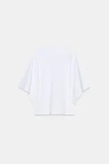 Camiseta blanca de manga corta con corte oversize y cuello redondo. El diseño presenta mangas amplias tipo capa que caen desde el hombro.