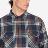 Camisa de manga larga con estampado a cuadros en tonos marrón, azul y celeste. Tiene dos bolsillos en el pecho con cierre de botón.