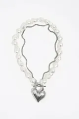 Collar de doble cadena, una compuesta por perlas barrocas y otra de eslabones metálicos finos, unidas por un dije central en forma de corazón plateado con cierre tipo barra.