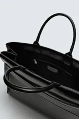 Bolso de mano de gran tamaño en color negro, con diseño estructurado, doble asa superior y cierre magnético. Incluye detalles de cintas laterales y compartimentos internos con cierre.
