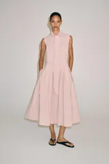 Vestido midi de Zara Woman Collection color rosado, confeccionado en hilatura de algodón. Presenta cuello subido con lazada, diseño sin mangas, bolsillos laterales ocultos y pliegues delanteros. Su falda tiene acabado en línea evasé y cuenta con cierre frontal mediante botones ocultos por solapa.