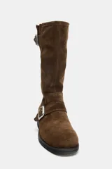 Botín plano de estilo motero en serraje color marrón, con punta redonda. Presenta dos tiras con hebillas metálicas, una en la caña y otra en el empeine. La suela tiene una altura de 4 cm.