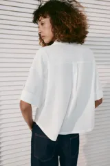 Camisa crop de mezcla de lino color blanco, con cuello solapa, escote en V, manga corta con trabilla, bolsillos de plastrón en el delantero y cierre frontal de botones.