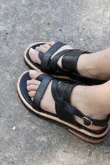 Sandalias bajas de cuero sintético color negro, con tiras cruzadas y hebilla lateral.