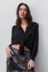 Camisa de manga larga color beige con cuello clásico y botonadura frontal. Presenta mangas con volumen sutil, puños abotonados y una silueta amplia de caída fluida.