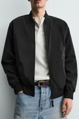 Cazadora bomber ligera de tejido técnico color verde oliva, con cuello, puños y bajo en rib elástico. Presenta cierre frontal de cremallera y bolsillos de vivo en la cadera.