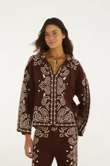 Sweater de punto color marrón con diseño estampado estilo paisley en tono crudo, cuello camisero con escote en V y cordones decorativos, mangas largas y calce amplio.