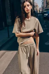 Pantalón de algodón color beige con tiro medio, cintura elástica ajustable con cordón y perneras anchas con pliegues delanteros y bolsillos laterales.