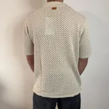 Camisa de tejido de punto calado en color beige, con cuello polo, cierre frontal de botones y mangas cortas.