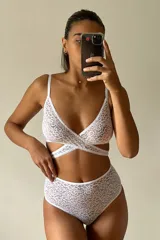 Conjunto de lencería de encaje blanco, compuesto por un corpiño triangular con diseño cruzado en la parte inferior y una bombacha de tiro alto.
