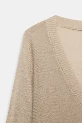 Jersey de punto metalizado color beige, con escote en V y manga larga.