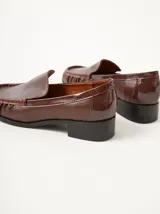 Mocasines de cuero negro con costuras pespunteadas en hilo blanco a contraste, diseño fruncido en la puntera, talón plano con pequeño tacón y apliques sutiles en charol.