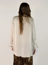 Camisa de satén color negro con cuello mao y volados en las mangas. Presenta cierre frontal con botones y diseño de corte holgado con largo asimétrico.