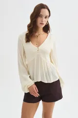 Blusa blanca de viscosa, con cuello en V, detalles de frunces en el frente, botones decorativos y mangas largas holgadas.