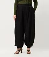 Pantalón de corte aladín confeccionado en crepé, de tiro alto con cintura elástica en la parte trasera. Presenta piernas anchas con volumen tipo globo que se estrechan en los tobillos mediante puños elásticos. Incluye bolsillos laterales funcionales.