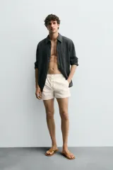 Short de baño en tejido técnico color beige claro, con cintura elástica ajustable con cordón y botón, bolsillos laterales y detalle de costuras en contraste.