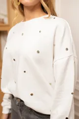 Sweater de corte oversize color beige, confeccionado en algodón. Presenta un diseño holgado con cuello redondo, puños y ruedo acanalados, decorado con múltiples apliques metálicos circulares en tonos dorados y plateados distribuidos por toda la prenda.