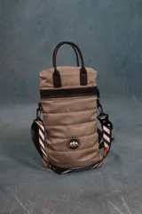 Matera estilo mochila color verde militar, confeccionada en nylon acolchado con detalles en símil cuero negro. Cuenta con tapa con cierre metálico, bolsillo interno, asas de mano y correa extensible para llevar al hombro o cruzada.