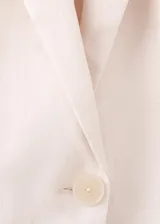 Blazer de lino color beige, de diseño recto con cuello en V, solapas con muesca, mangas largas, bolsillos de ribete delanteros y cierre frontal de un botón.