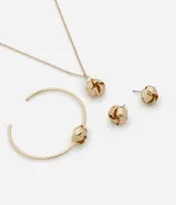 Conjunto de bisutería compuesto por un collar con dije de nudo, un par de aros tipo botón con diseño de nudo y una pulsera rígida abierta con detalle de nudo central. Todas las piezas presentan un acabado metálico dorado.