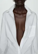 Camisa blanca de popelina de algodón con cuello camisero, cierre de botones, manga larga y detalles fruncidos.