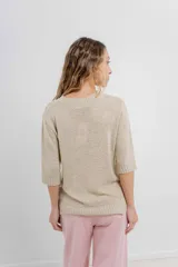 Buzo de tejido abierto color beige claro, de calce oversize con mangas 3/4 y cuello redondo. Presenta terminaciones acanaladas en puños y cintura.