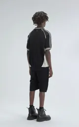 Chomba tejida de hilo color negro con punto cerrado, cuello polo con escote en V y ribetes blancos en cuello y mangas. Presenta bordados en blanco: un número "90" y la palabra "Ravers" en cursiva.