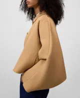 Chaqueta corta de color camel confeccionada en mezcla de lana y poliéster. Presenta cuello de solapa, manga larga de estilo japonés, cierre frontal con botones a tono y bolsillos laterales. Incluye un detalle de capa superpuesta en la espalda.