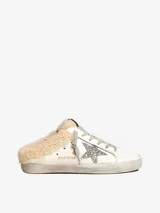 Zapatilla deportiva de cuero blanco con cordones grises, detalle de estrella plateada con glitter en el lateral y forro de lana color crema.