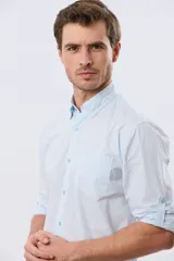 Camisa celeste de manga larga confeccionada en algodón, con cuello camisero, cierre frontal de botones, bolsillo en el pecho y diseño de cuadros sutiles.
