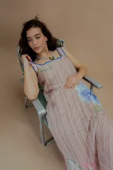 Vestido largo de tejido calado color beige, con estampado de flores en tonos rosados, celestes y verdes. Presenta escote cuadrado con ribete azul y terminaciones con crochet fucsia.