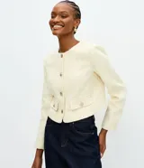Campera tipo chaquetilla confeccionada en tweed de poliéster, con cuello redondo, manga larga y corte corto. Presenta cierre frontal mediante botones metálicos y cuatro bolsillos delanteros aplicados con solapa.