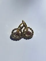 Aros colgantes con forma circular, con strass plateado alrededor y flor de vidrio amarilla con centro rojo en el interior. El arito es de acero quirúrgico.