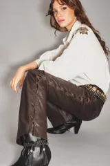 Pantalon de cuero ovino color marron, de corte bootcut, con detalle de cordones cruzados a lo largo de las costuras laterales y cierre de ojalillos metalicos.