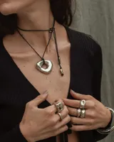 Collar con dije de forma irregular en tonos dorados y plateados, suspendido de un cordón doble de algodón negro.