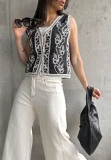 Chaleco negro con bordado floral blanco, escote en V, cierre frontal con botones y ribete de encaje.