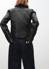 Chaqueta estilo biker de cuero sintético negro, con cierre frontal cruzado, solapas con muesca y broches metálicos.