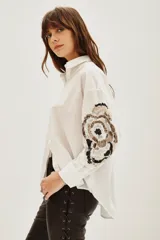 Camisa blanca de algodón con mangas largas, destacada por bordados decorativos en color negro y plateado en las mangas.