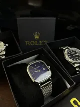 Reloj Casio Quartz con caja cuadrada plateada, esfera azul intenso, manecillas y marcadores de hora dorados, y correa de acero inoxidable plateada. Incluye función de fecha.