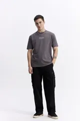 Remera de manga corta color gris oscuro, con escote redondo y fit regular. Presenta un estampado frontal con el texto "new season designed and produced by mistral".