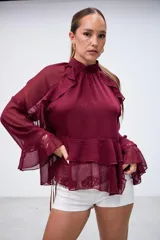 Blusa color bordó con cuello alto, mangas largas acampanadas y detalles de volados en el pecho y el ruedo.
