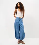 Pantalón de jean estilo aladín con tiro medio, cintura con pasadores, cierre frontal con botón y bolsillos funcionales. Presenta un calce amplio con diseño tipo globo y terminación ajustada en los puños.